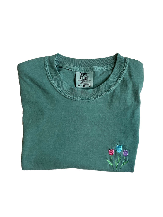 green t-shirt with pink, blue and purple embroidery of tulips